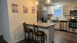 Una cocina con una isla central, taburetes de bar, electrodomésticos de acero inoxidable y suelo de madera.
