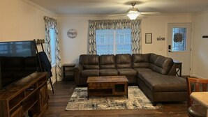 Una sala de estar con un sofá modular, una mesa de centro, un televisor y un ventilador de techo.