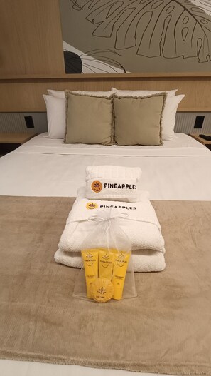 Ein Hotelzimmer mit einem Bett, zwei Kissen, einem gefalteten Handtuch und einer Reihe von Pflegeprodukten.