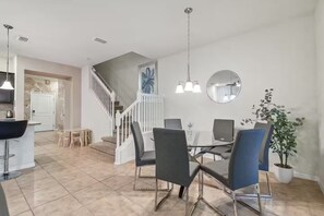 A modern dining area with a glass table, black and blue chairs, and pendant lighting. - 5 bdrm Pet friendly, private pool, comm. waterpark (Davenport)