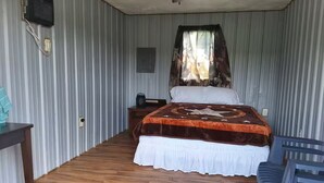 A bedroom with a bed, a nightstand, a desk, and a chair. - Arabian Cabin (Heavener)