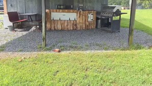 A small outdoor kitchen area with a grill, a sink, and a wooden counter. - Arabian Cabin (Heavener)