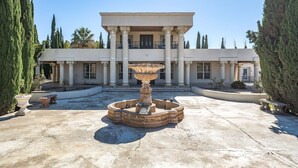 Un imposant bâtiment doté d’une fontaine centrale, entouré de colonnes disposées de manière symétrique et de cyprès.