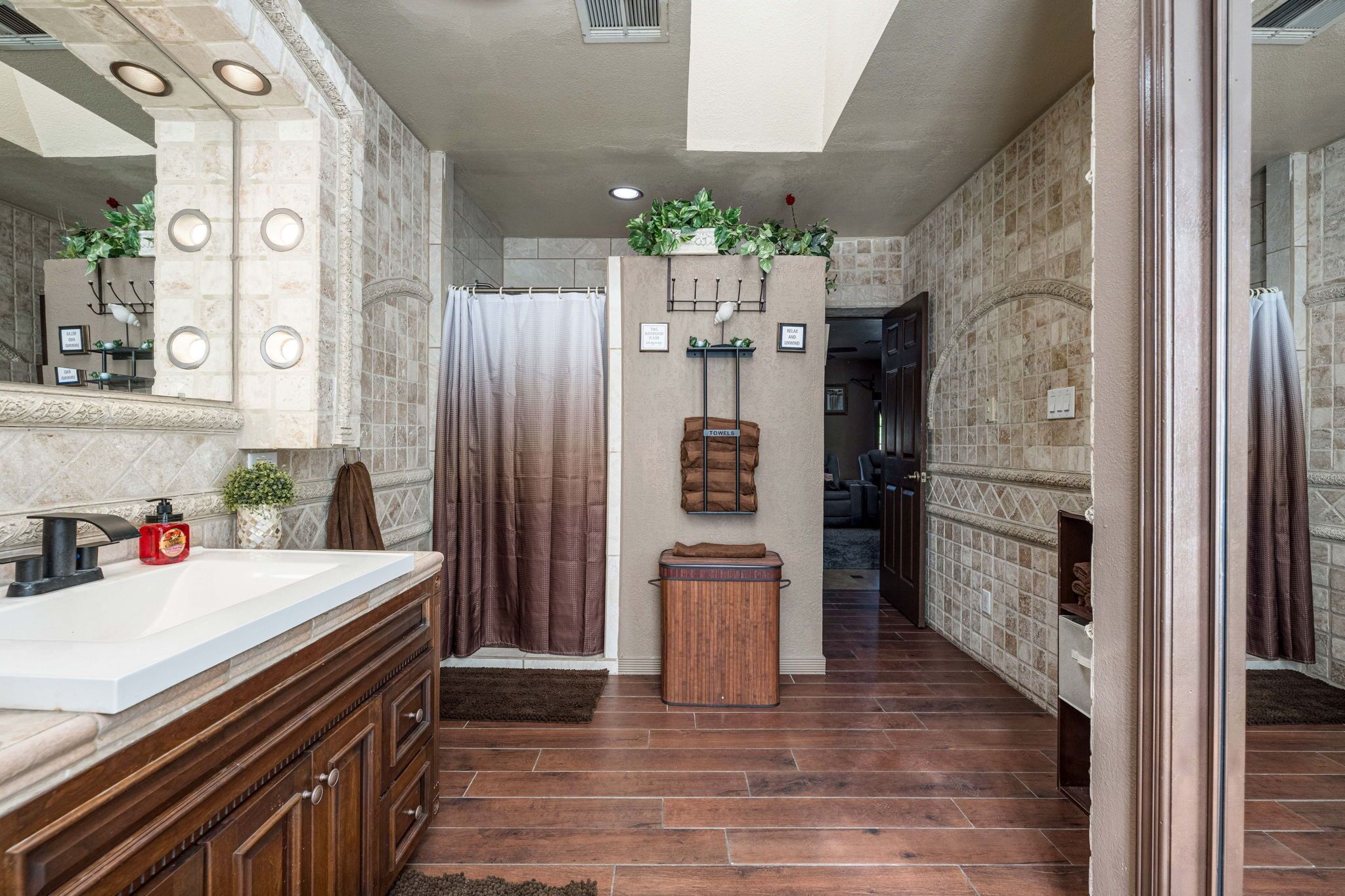 Une salle de bain avec un grand miroir, un lavabo, un rideau de douche et un meuble en bois.