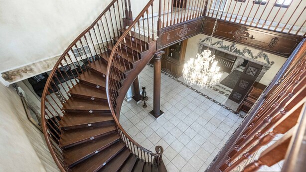 Un escalier en colimaçon avec des rampes en bois et un lustre dans la pièce adjacente.
