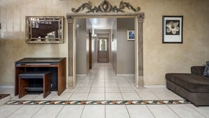 Un couloir avec un sol carrelé, une console en bois, un miroir encadré et un tableau encadré accroché au mur.