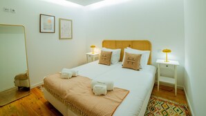 A neatly arranged hotel room with a large bed, two bedside tables with lamps, a small stool, and a mirror. - VIVA República Serviced Apartment -1T (Porto)