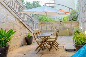 An outdoor patio with a stone wall, a wooden table and chairs, potted plants, and a large umbrella. - VIVA República Serviced Apartment -1T (Porto)