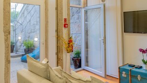 A modern room with a glass door leading to a courtyard, a sofa, a small table with a vase, and a mounted TV. - VIVA República Serviced Apartment -1T (Porto)
