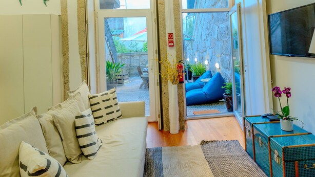 A cozy room with a sofa, a small table with a vase, and a TV on the wall. - VIVA República Serviced Apartment -1T (Porto)