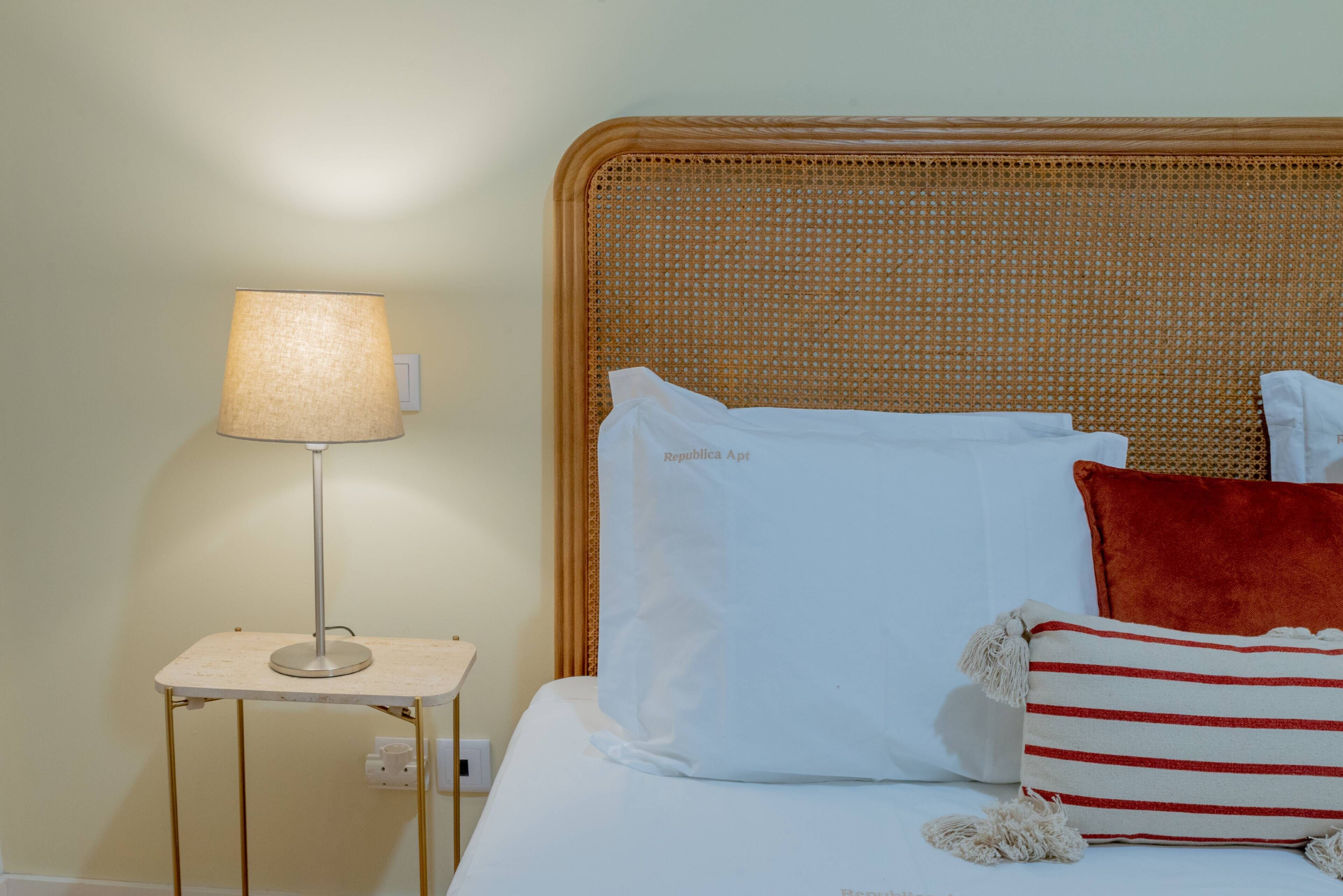 Una cama bien hecha con ropa blanca y una almohada a rayas rojas y blancas.