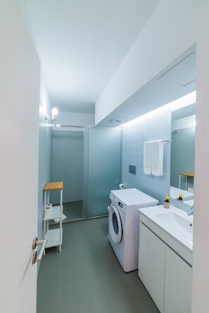 A compact bathroom with a washing machine, a sink, a mirror, and a towel rack. - VIVA República Serviced Apartment 1F (Porto)