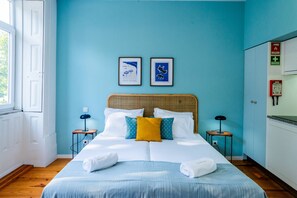 A hotel room with a bed, two framed pictures on the wall, a window, and a door. - VIVA República Serviced Apartment 1F (Porto)