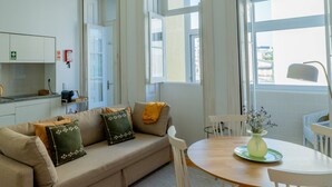 A modern living room with a beige sofa, a wooden dining table, and a vase of flowers. - VIVA República Serviced Apartment 1T (Porto)