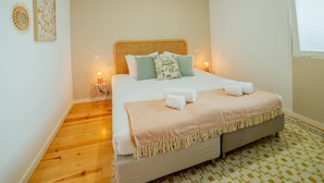 A neatly made bed with a wooden headboard, two bedside lamps, and a patterned rug on a wooden floor. - VIVA República Serviced Apartment 1T (Porto)