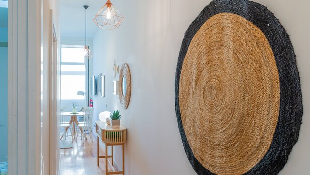 A hallway with a large woven wall hanging, a hanging light fixture, and a small wooden table with a plant. - VIVA República Serviced Apartment 1T (Porto)