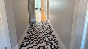 Un couloir doté d’un sol à motifs géométriques, de murs blancs et d’une porte donnant sur une pièce avec vue.
