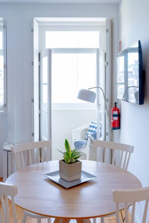 A round wooden table with white chairs, a potted plant, and a fire extinguisher mounted on the wall. - VIVA República Serviced Apartment 2T (Porto)