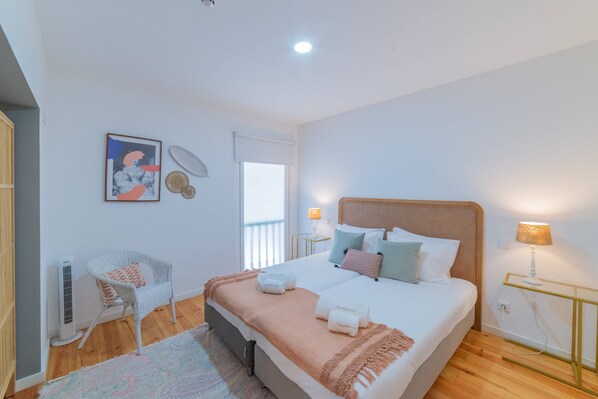 A bedroom with a large bed, a chair, a bedside table, a lamp, and a window. - VIVA República Serviced Apartment 2T (Porto)