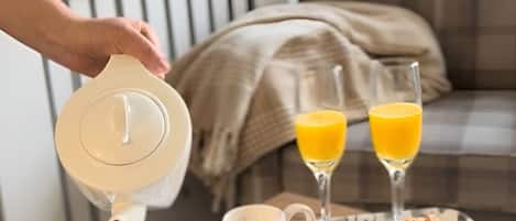 Bandeja de desayuno con cruasanes, dos vasos de jugo de naranja y dos tazas blancas sobre una mesa de madera.