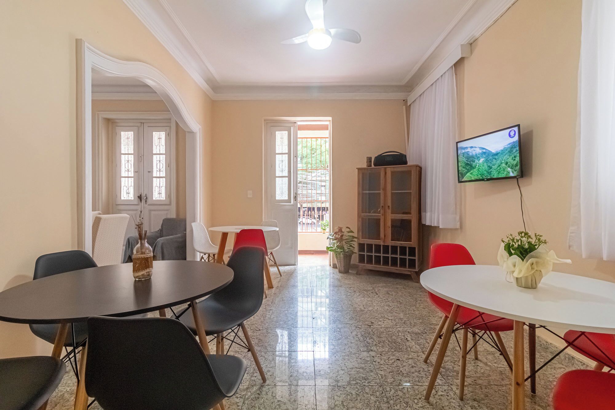 Un coin repas avec une table ronde et des chaises, un téléviseur fixé au mur et une vue sur l’extérieur par une fenêtre.