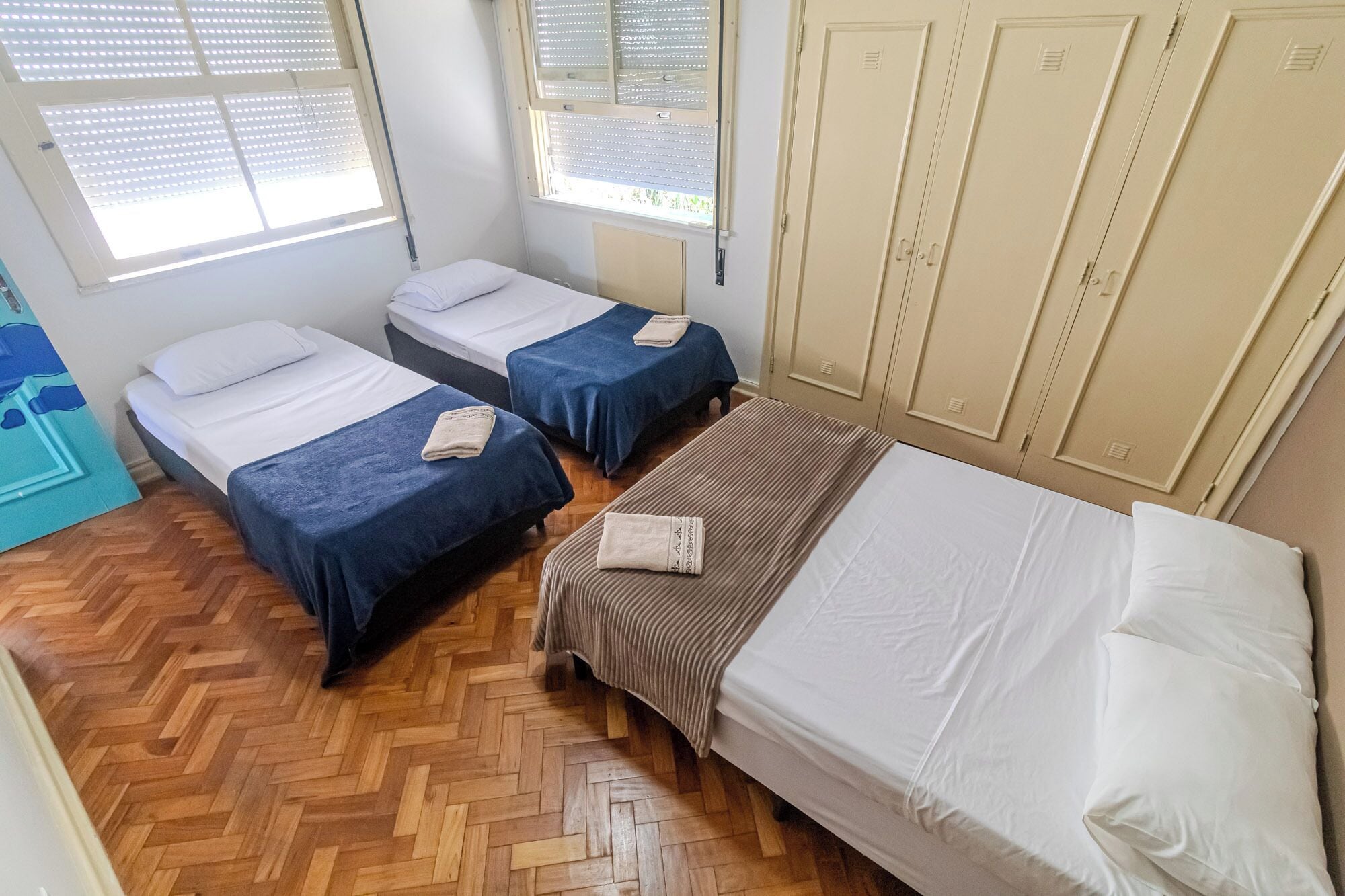 Una habitación con dos camas individuales, una cama más grande, suelo de madera y un armario con varias puertas.