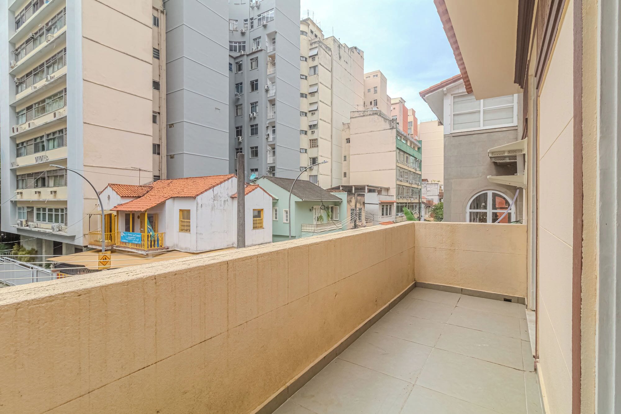 A narrow balcony with a tiled floor, bordered by a beige wall and adjacent buildings.
