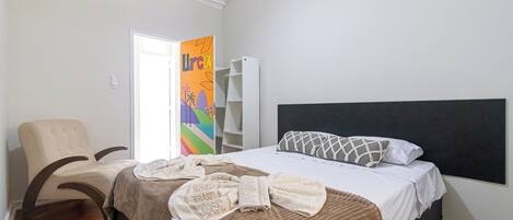 Un dormitorio con cama, una silla, un armario y una puerta con un mural colorido.