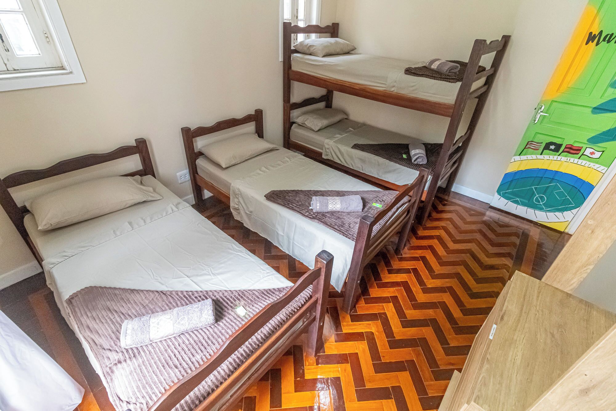 Una habitación con cuatro camas literas de madera, suelo de madera con un patrón de espiga y un adorno de pared colorido.