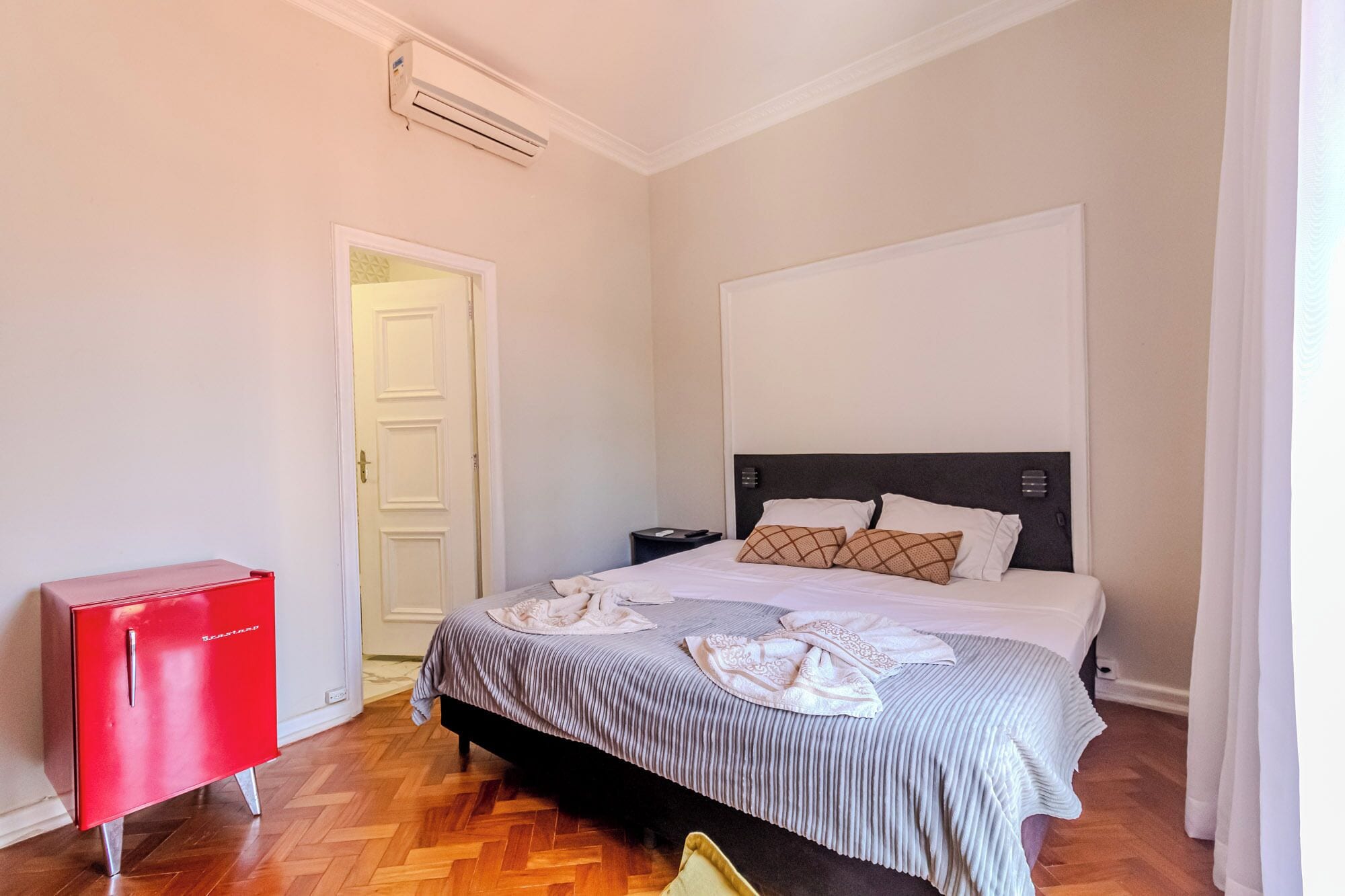 Un dormitorio con una cama, un armario rojo, una mesita de noche y un equipo de aire acondicionado.