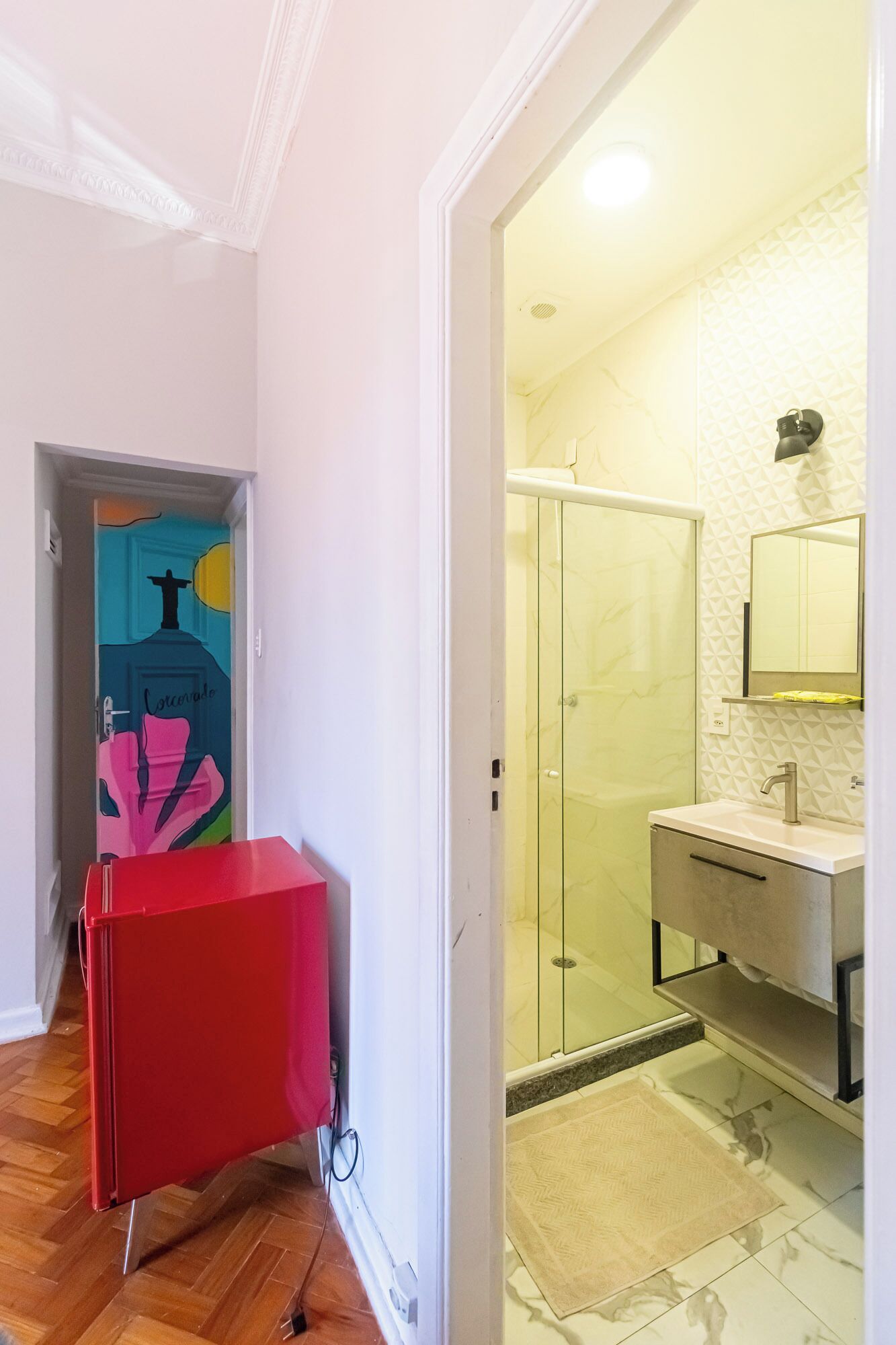 Un pasillo que conduce a un baño con ducha de vidrio, lavamanos y espejo.