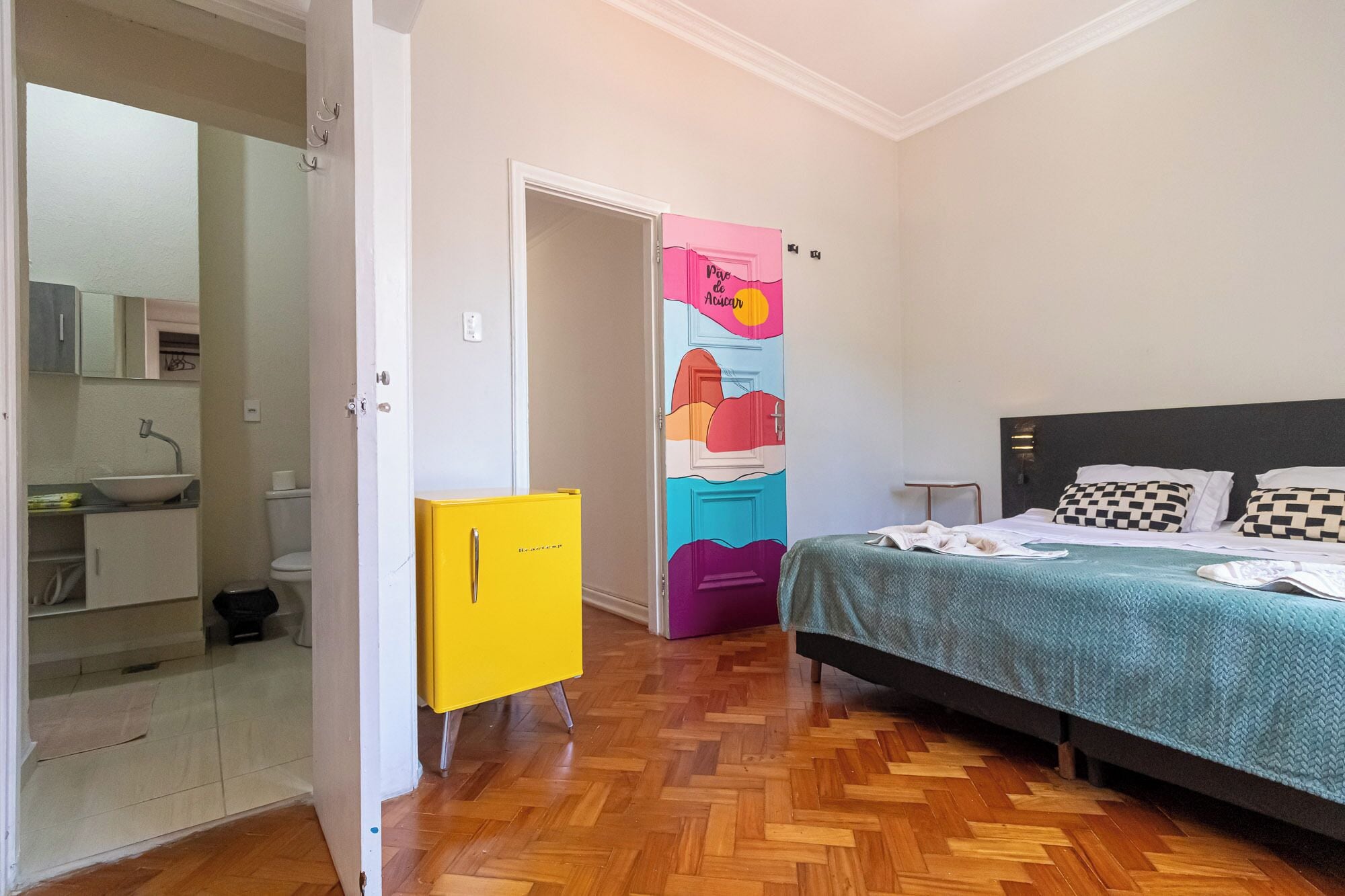 Une chambre à coucher comprenant un lit, une table de chevet, une commode et une porte ornée d’œuvres d’art colorées.