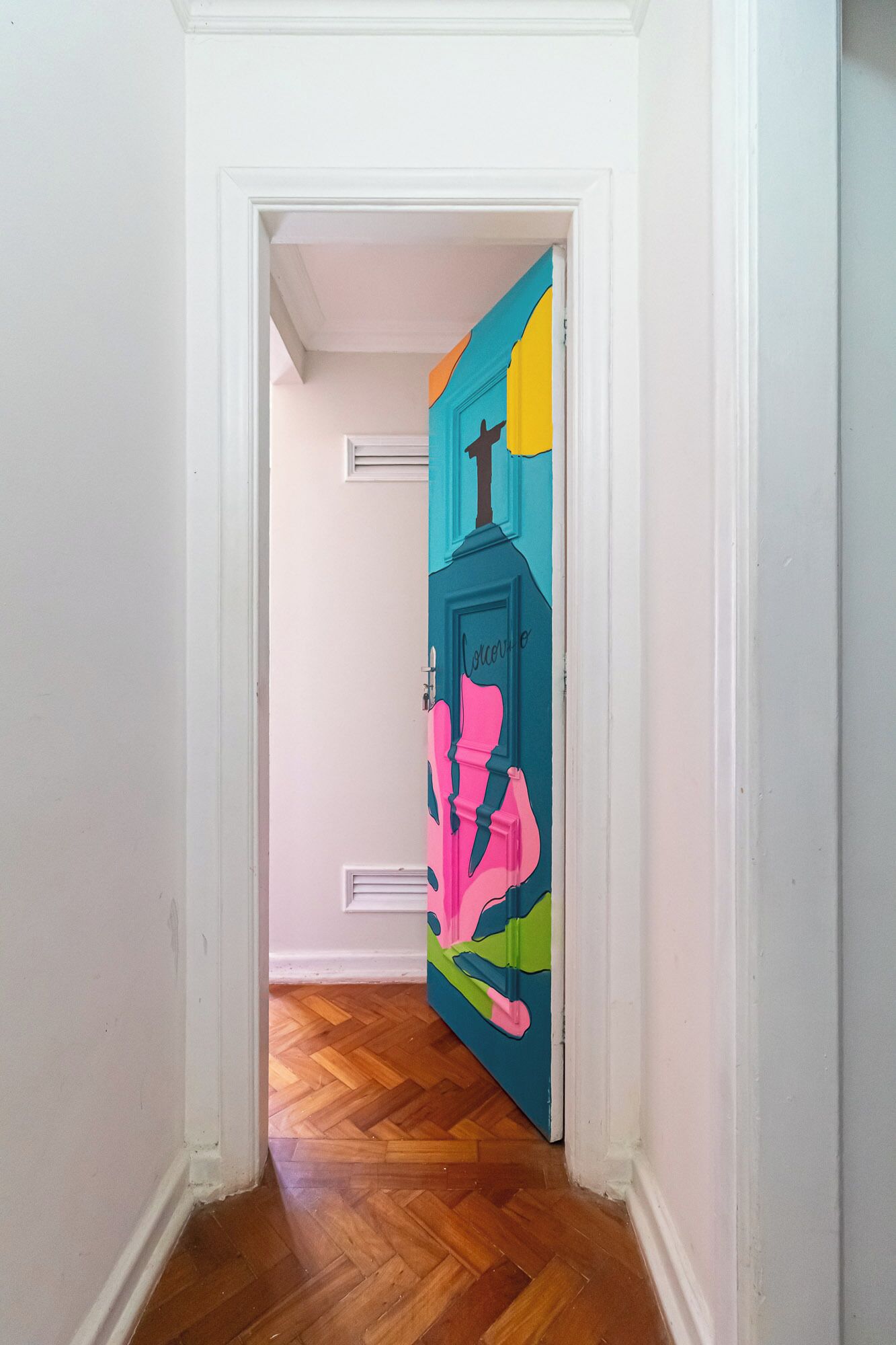 Un pasillo con suelo de madera y una puerta decorada con un mural colorido.