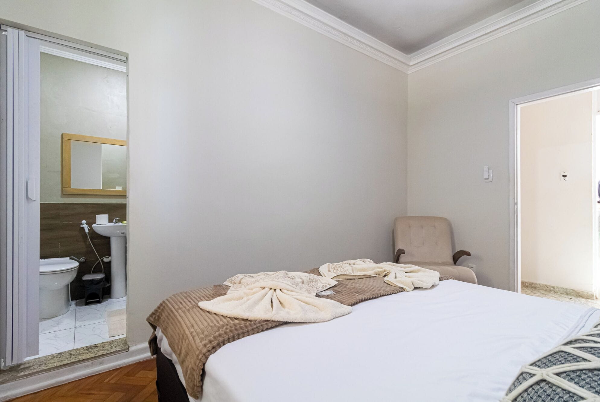 Une chambre à coucher avec un lit, une chaise, une salle de bain avec des toilettes et un lavabo, et un miroir.