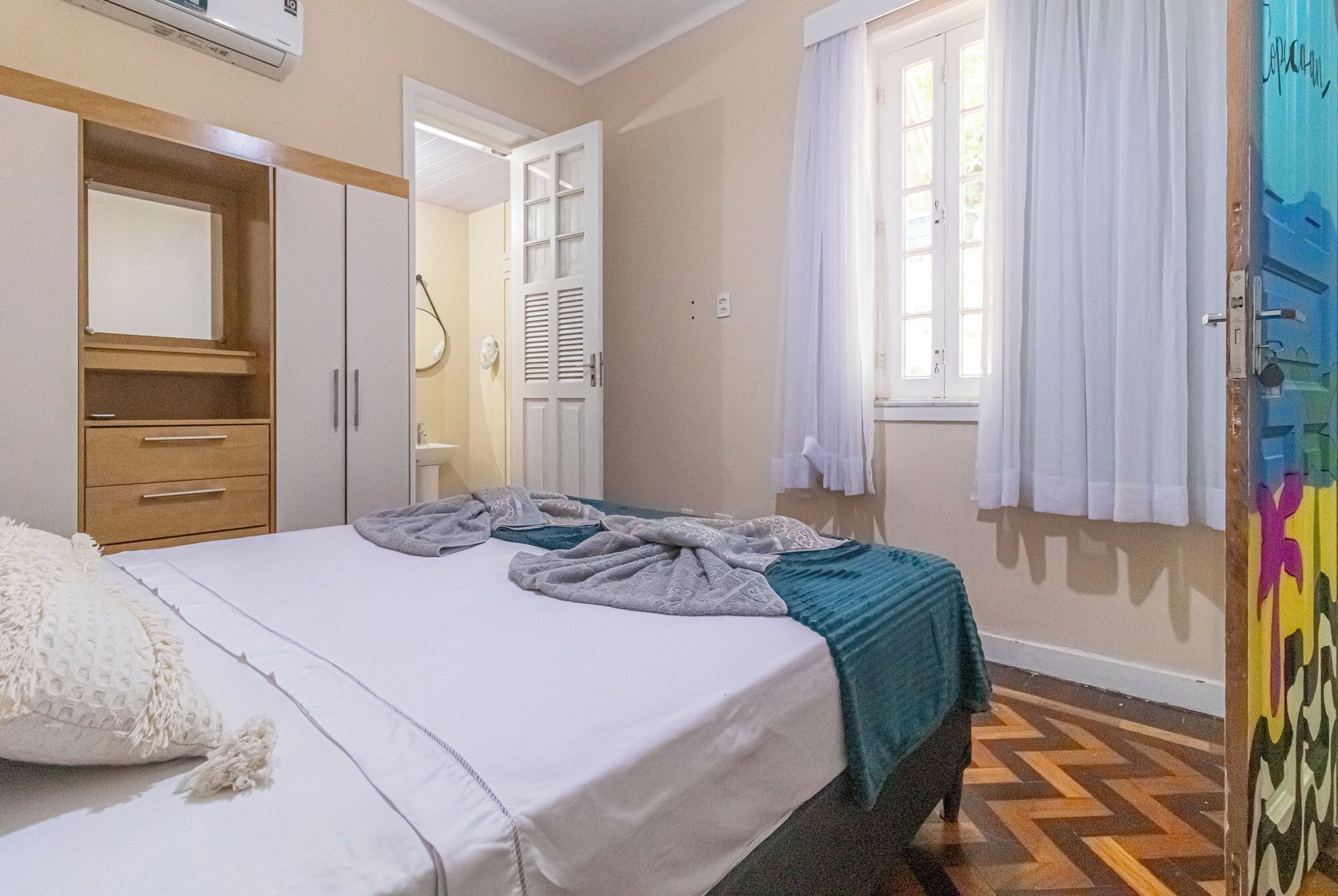 A bedroom with a bed, a wardrobe, a bathroom, and a window with curtains.