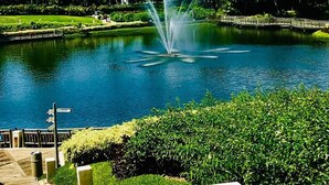 Un parc paisible avec une fontaine, une végétation luxuriante et une promenade en bois.