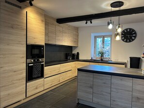 Eine moderne Küche mit Holzschränken, einem eingebauten Ofen, einer Mikrowelle und einer großen Kücheninsel mit Spüle.