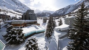 Une station de montagne enneigée, avec des bâtiments modernes, un pont de verre et des arbres chargés de neige.