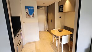 Un couloir étroit mène à un coin repas où se trouvent une table en bois et des chaises blanches, un four à micro-ondes placé au-dessus de la table, et une affiche accrochée au mur.