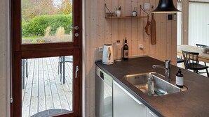 A modern kitchen with a wooden interior, a built-in dishwasher, a sink with a faucet, and a window overlooking a garden. - Beautiful home in Gilleleje with WiFi (Gilleleje)