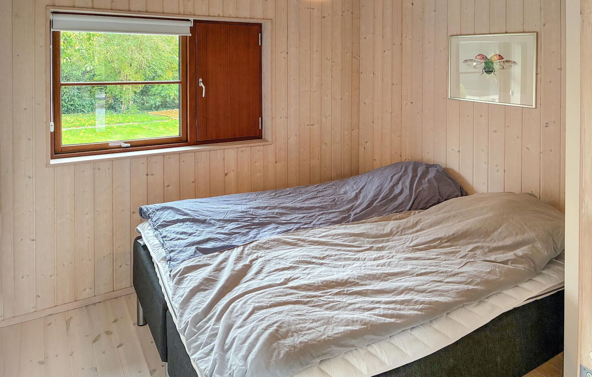 Un letto singolo in una stanza con pareti in legno, una finestra con persiana di legno e un quadro appeso al muro.