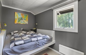 Un dormitorio con cama, ventana con vistas a árboles, radiador y un cuadro en la pared.