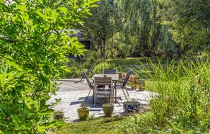 Una terraza de madera al aire libre con una mesa y sillas, rodeada de exuberante follaje y árboles.