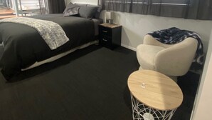 A modern hotel room with a large bed, a small desk, a chair, and a window with curtains.