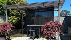 A patio area with a covered table and chairs, surrounded by potted plants and a pergola.