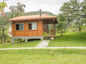 A wooden cabin with a tiled roof, a porch, and a small garden area. - Pousada Fazenda Caetés (Camboriu)