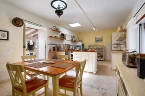 A dining area with a wooden table and chairs, a kitchen with white cabinets and shelves, and a view through an open doorway. - Casa del Valle – rural oasis with private pool and charm (Betancuria)