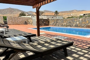 A pool area with lounge chairs and a pergola, surrounded by stone walls and a mountainous backdrop. - Casa del Valle – rural oasis with private pool and charm (Betancuria)