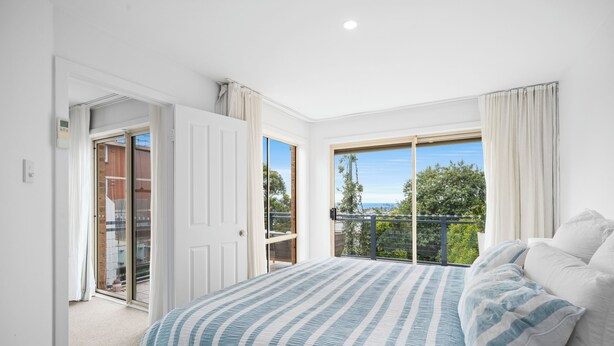 Un dormitorio con una cama grande, una puerta corrediza al balcón y vistas a zonas verdes.