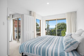 A bedroom with a large bed, a sliding glass door to a balcony, and a view of greenery. - Bondi Beach Views! Spacious and Convenient 4BR, 2BA House With Free Parking (Bondi)